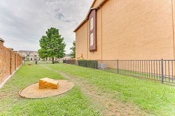 A large tan building with a black fence and a tree in front at Limestone Ranch Apartments, Lewisville, TX, 75067